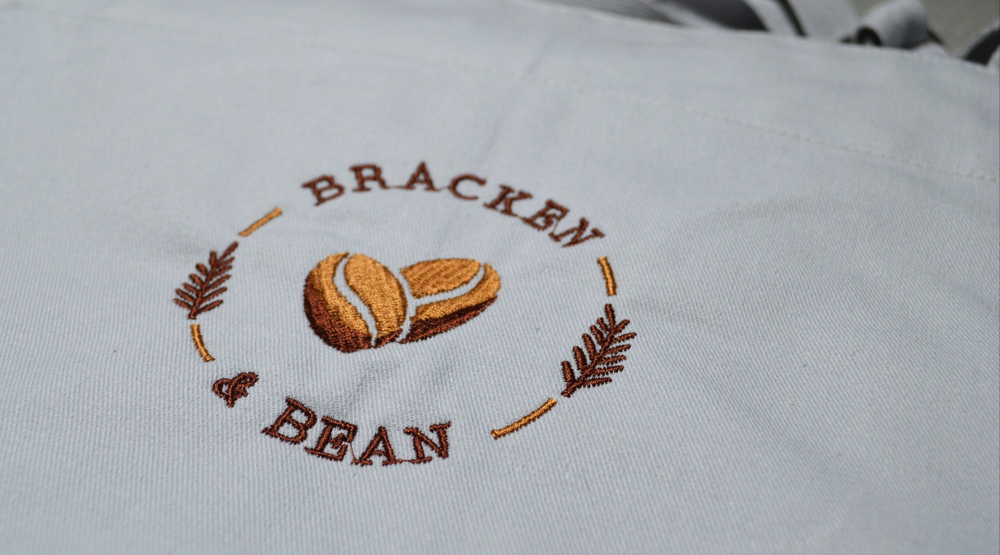 White apron with embroidered 'Bracken & Bean' logo on a white background