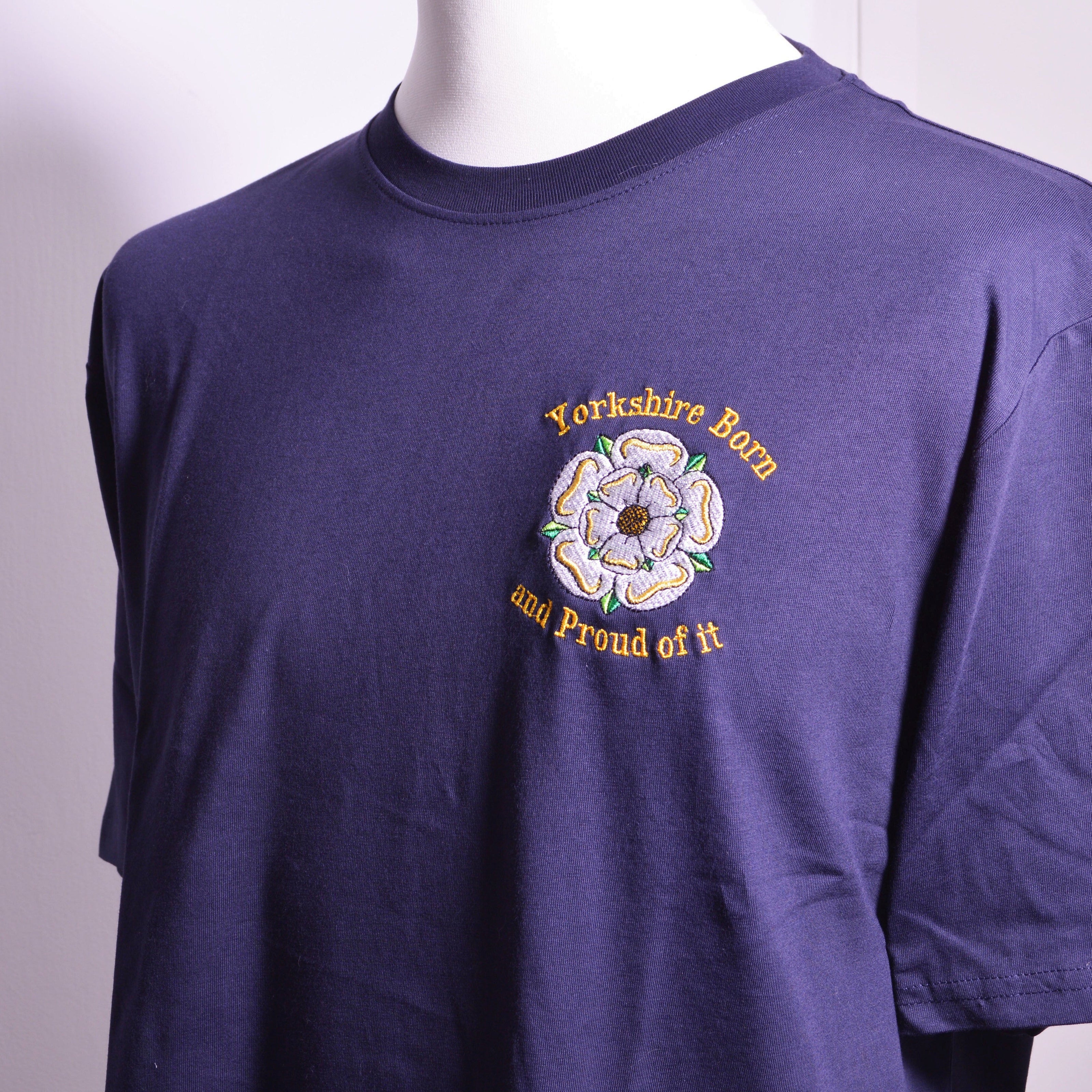 A navy blue short-sleeve t-shirt displayed on a white mannequin torso. On the left breast is an embroidered design featuring the yorkshire rose and yellow text reading "Yorkshire Born And Proud of It"
